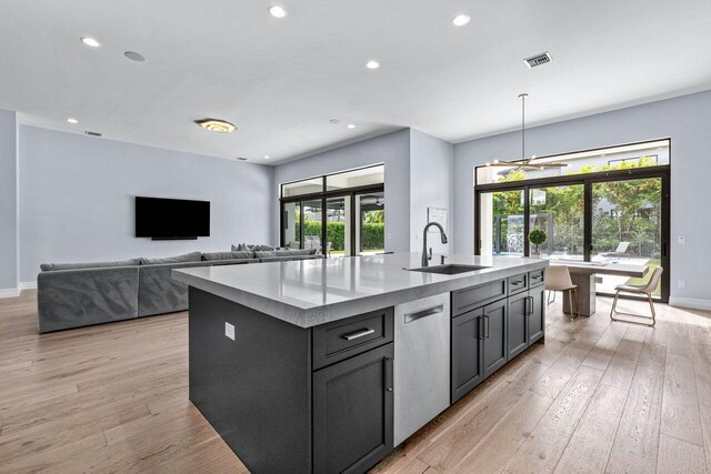 kitchen featuring sink, hanging light fixtures, stainless steel dishwasher, a center island with sink, and light wood-type flooring