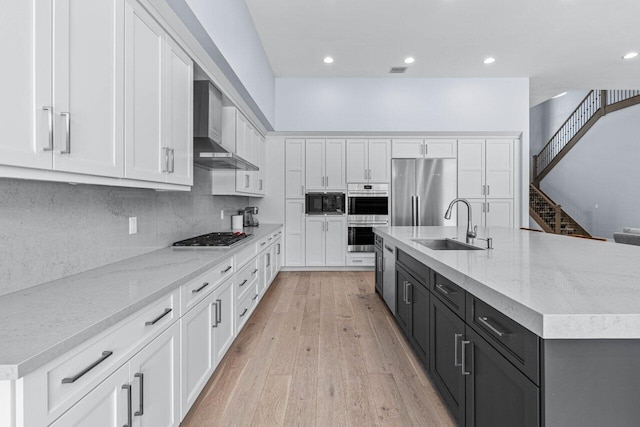 kitchen featuring built in appliances, white cabinetry, light wood-type flooring, and wall chimney range hood