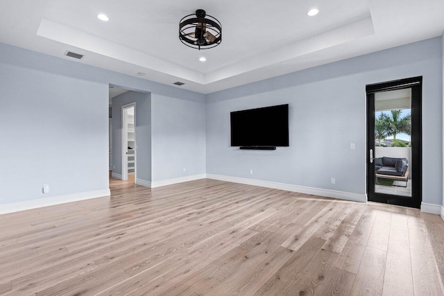 unfurnished living room featuring a tray ceiling and light hardwood / wood-style flooring