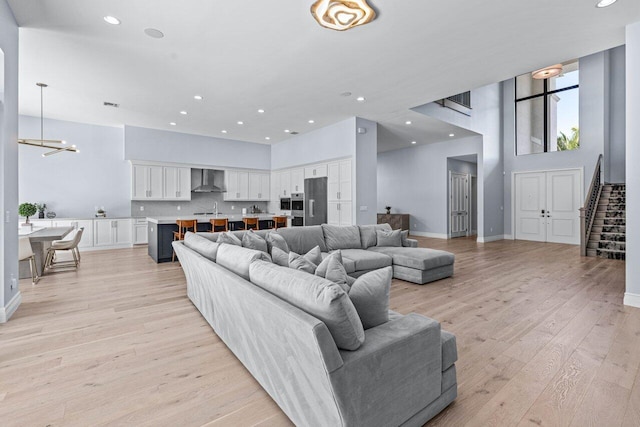 living room featuring sink, a towering ceiling, a chandelier, and light wood-type flooring