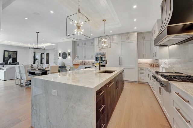 kitchen with light hardwood / wood-style floors, a large island with sink, appliances with stainless steel finishes, and light stone countertops