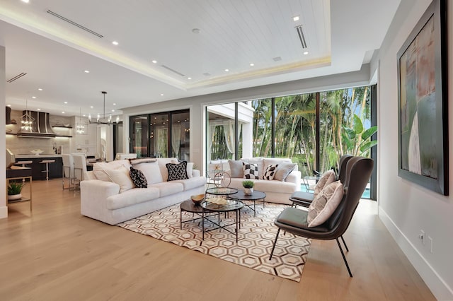 living room featuring light wood-style flooring, recessed lighting, a notable chandelier, baseboards, and a tray ceiling