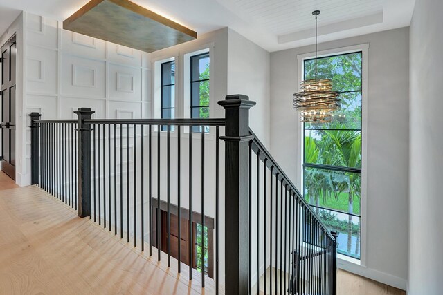 stairway featuring plenty of natural light, a tray ceiling, hardwood / wood-style floors, and a chandelier