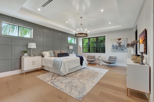 bedroom with light hardwood / wood-style floors, a raised ceiling, and an inviting chandelier