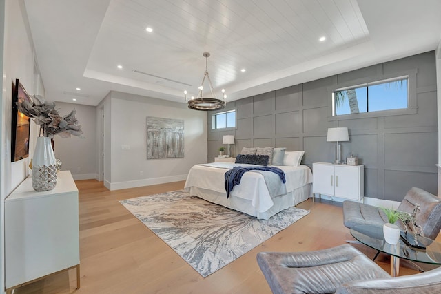 bedroom featuring a raised ceiling, light hardwood / wood-style floors, multiple windows, and a chandelier