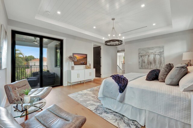 bedroom with a raised ceiling, access to outside, light hardwood / wood-style floors, and a chandelier