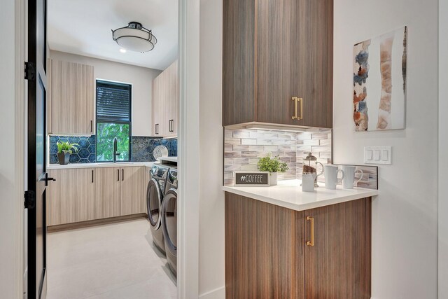 kitchen featuring tasteful backsplash, sink, washing machine and clothes dryer, light tile patterned floors, and kitchen peninsula