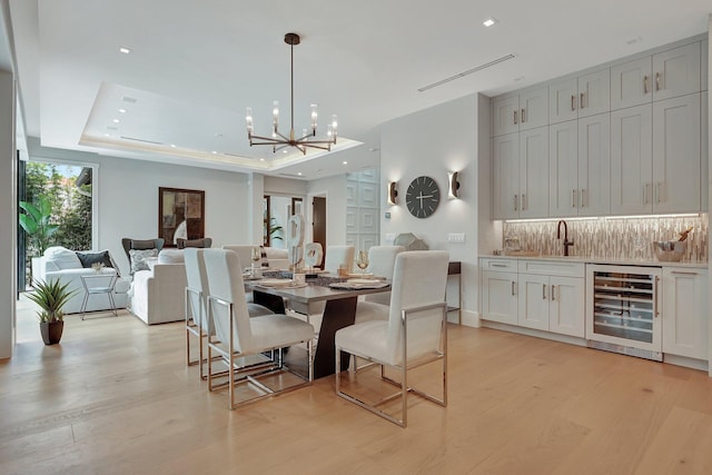 dining room featuring light wood-style floors, a tray ceiling, beverage cooler, and recessed lighting