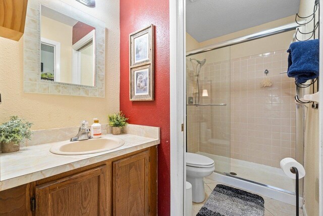 bathroom featuring an enclosed shower, vanity, tile patterned floors, and toilet