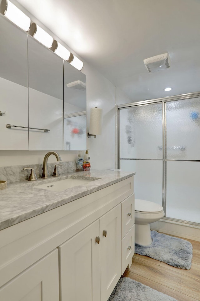 bathroom featuring hardwood / wood-style flooring, toilet, a shower with door, and vanity