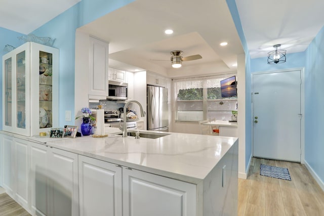 kitchen featuring white cabinets, stainless steel appliances, ceiling fan, kitchen peninsula, and light stone counters