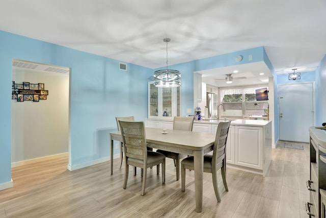 dining area featuring light hardwood / wood-style floors, sink, and ceiling fan with notable chandelier