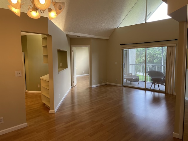 spare room with an inviting chandelier, a textured ceiling, hardwood / wood-style flooring, and lofted ceiling