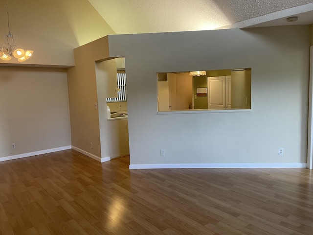 spare room with a textured ceiling, high vaulted ceiling, an inviting chandelier, and wood-type flooring