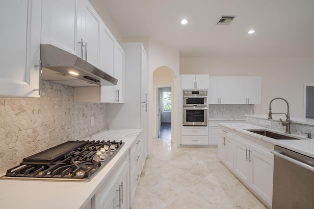 kitchen featuring stainless steel appliances, white cabinetry, light stone counters, and sink