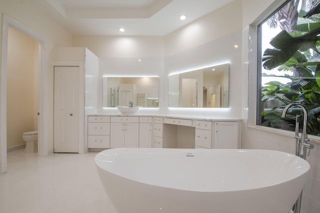 bathroom with vanity, tile walls, toilet, a bath, and a tray ceiling