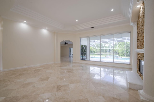 unfurnished living room featuring ceiling fan, a tray ceiling, crown molding, and a stone fireplace