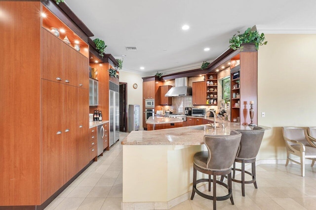 kitchen with kitchen peninsula, sink, light stone countertops, ornamental molding, and wall chimney exhaust hood