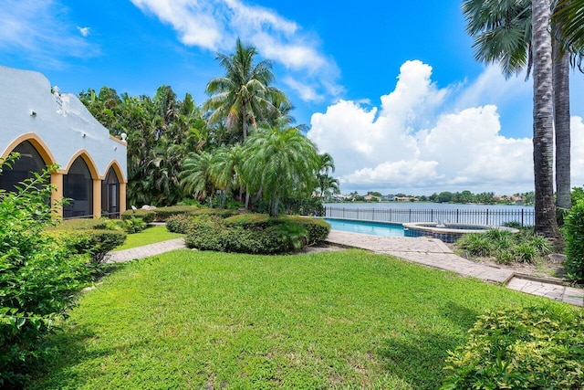 view of yard featuring a swimming pool with hot tub and a water view