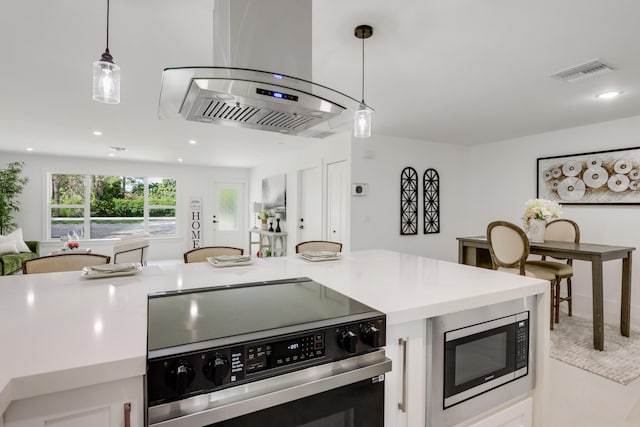 kitchen featuring electric range oven, white cabinetry, island exhaust hood, stainless steel microwave, and pendant lighting