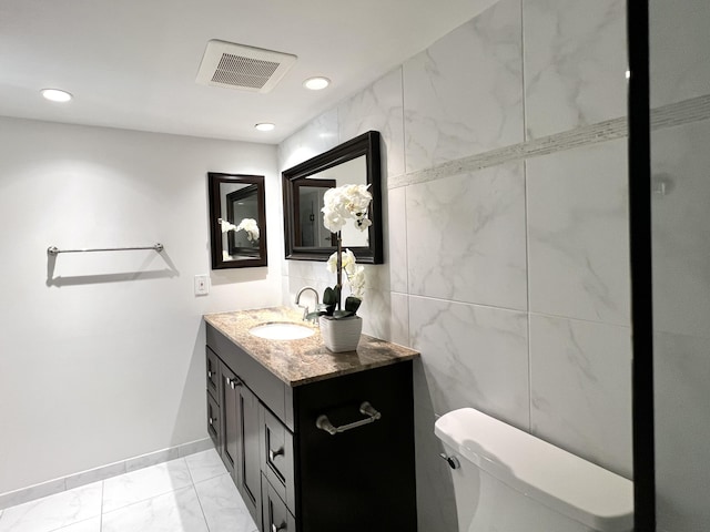 bathroom featuring vanity, tile walls, and toilet