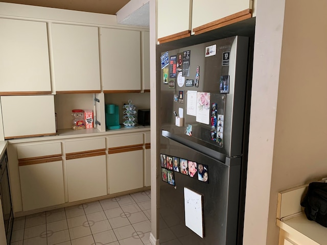 kitchen featuring light tile patterned flooring, stainless steel refrigerator, and white cabinets