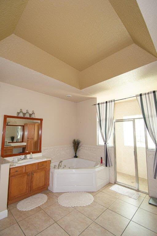 bathroom with a textured ceiling, vanity, vaulted ceiling, shower with separate bathtub, and tile patterned floors