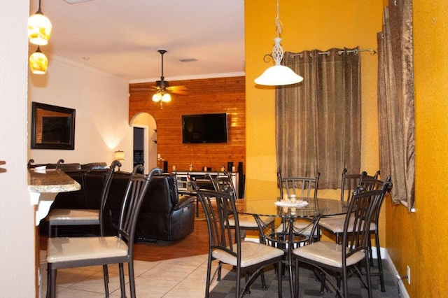 dining room featuring ceiling fan, ornamental molding, wooden walls, and light tile patterned flooring