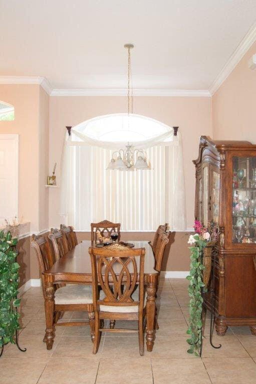 tiled dining area featuring crown molding and a notable chandelier