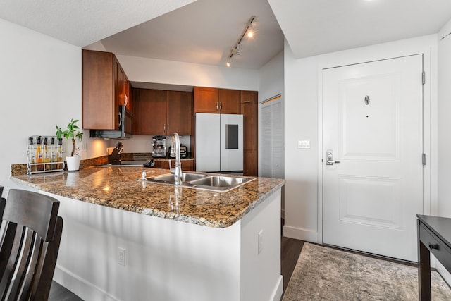 kitchen featuring stone counters, sink, white refrigerator, and kitchen peninsula