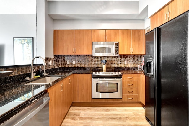 kitchen featuring appliances with stainless steel finishes, dark stone counters, light hardwood / wood-style floors, sink, and backsplash