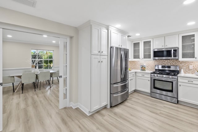 kitchen with stainless steel appliances, light wood-type flooring, white cabinets, and decorative backsplash