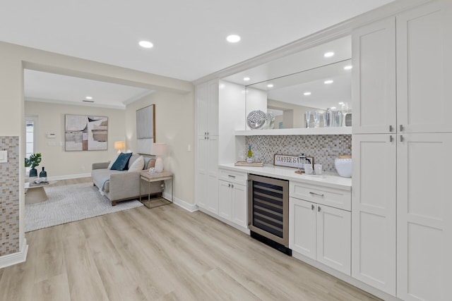 bar with beverage cooler, backsplash, ornamental molding, white cabinetry, and light wood-type flooring