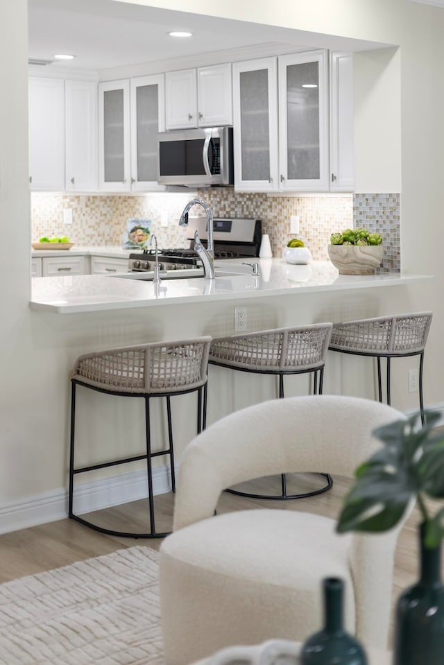 kitchen featuring light wood-type flooring, white cabinetry, tasteful backsplash, a kitchen breakfast bar, and appliances with stainless steel finishes