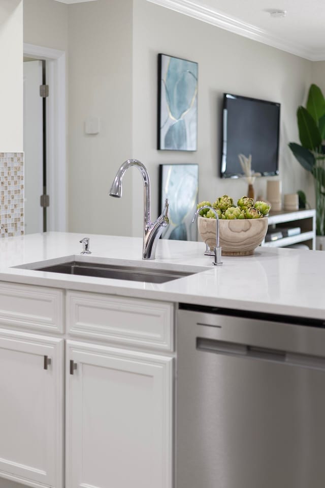 kitchen with crown molding, backsplash, sink, stainless steel dishwasher, and white cabinets