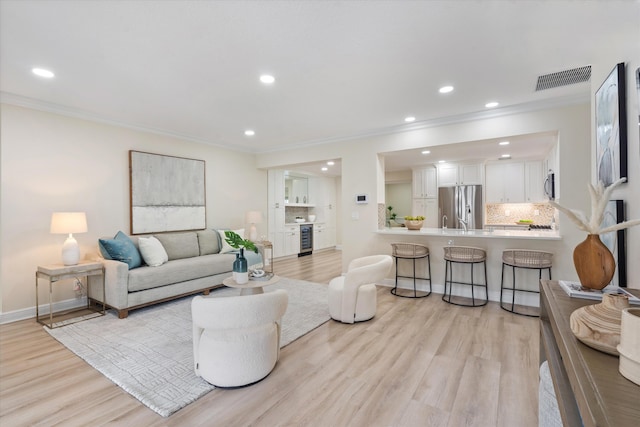 living room featuring ornamental molding, beverage cooler, and light hardwood / wood-style floors