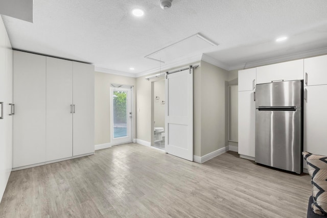 kitchen with stainless steel fridge, crown molding, a barn door, light wood-type flooring, and white cabinets