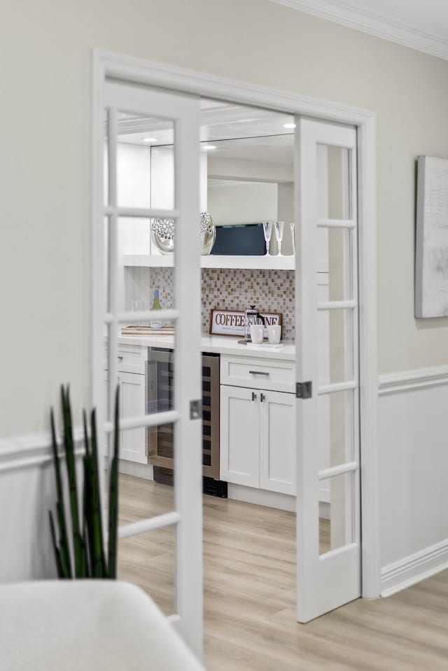 bar featuring wine cooler, light hardwood / wood-style floors, crown molding, decorative backsplash, and white cabinetry