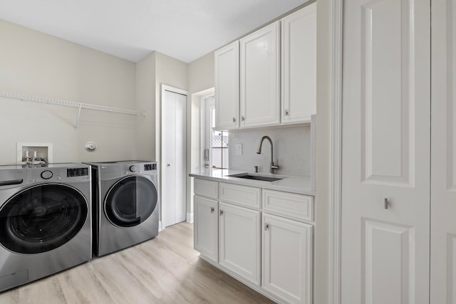 clothes washing area featuring washing machine and dryer, cabinets, sink, and light wood-type flooring