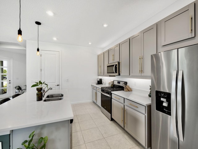 kitchen featuring an island with sink, stainless steel appliances, hanging light fixtures, sink, and gray cabinetry