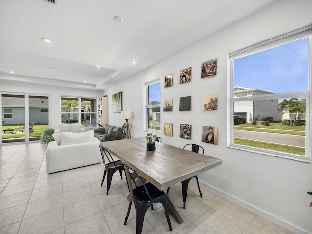 tiled dining space with a tray ceiling and a healthy amount of sunlight