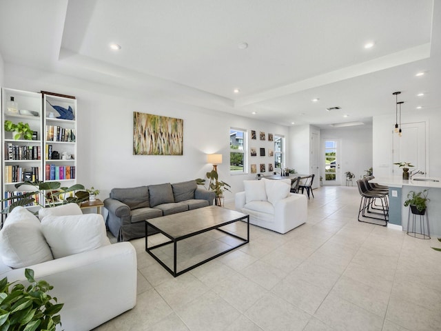 living room featuring a healthy amount of sunlight, a raised ceiling, sink, and light tile patterned floors