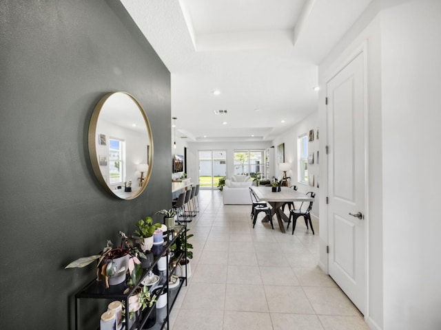 hall featuring light tile patterned floors and a tray ceiling