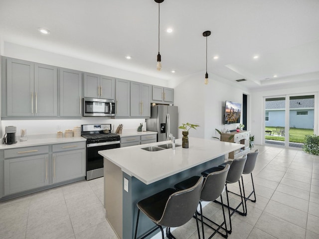 kitchen with light tile patterned flooring, a breakfast bar area, stainless steel appliances, hanging light fixtures, and a center island with sink