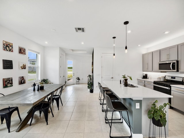 kitchen featuring stainless steel appliances, sink, light tile patterned floors, and an island with sink