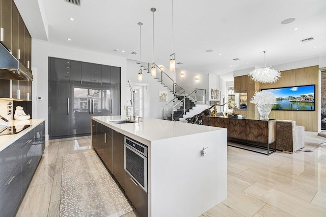 kitchen featuring black electric cooktop, a large island with sink, hanging light fixtures, oven, and a notable chandelier