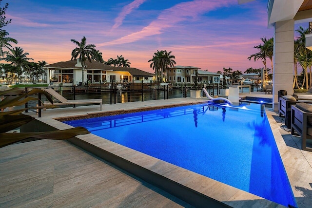 pool at dusk featuring a water view, a water slide, and a boat dock