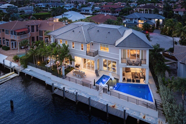 back of property with a water view, a balcony, and a patio area