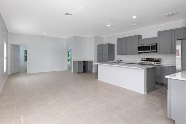 kitchen featuring gray cabinetry, light tile patterned floors, stainless steel appliances, a kitchen island with sink, and sink