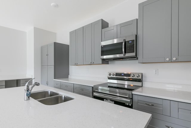 kitchen with light stone counters, stainless steel appliances, sink, and gray cabinetry